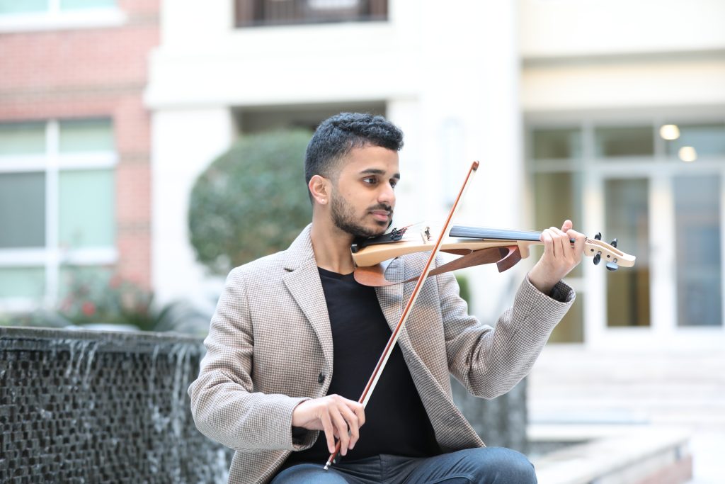 Achi Bala playing violin seated in a courtyard