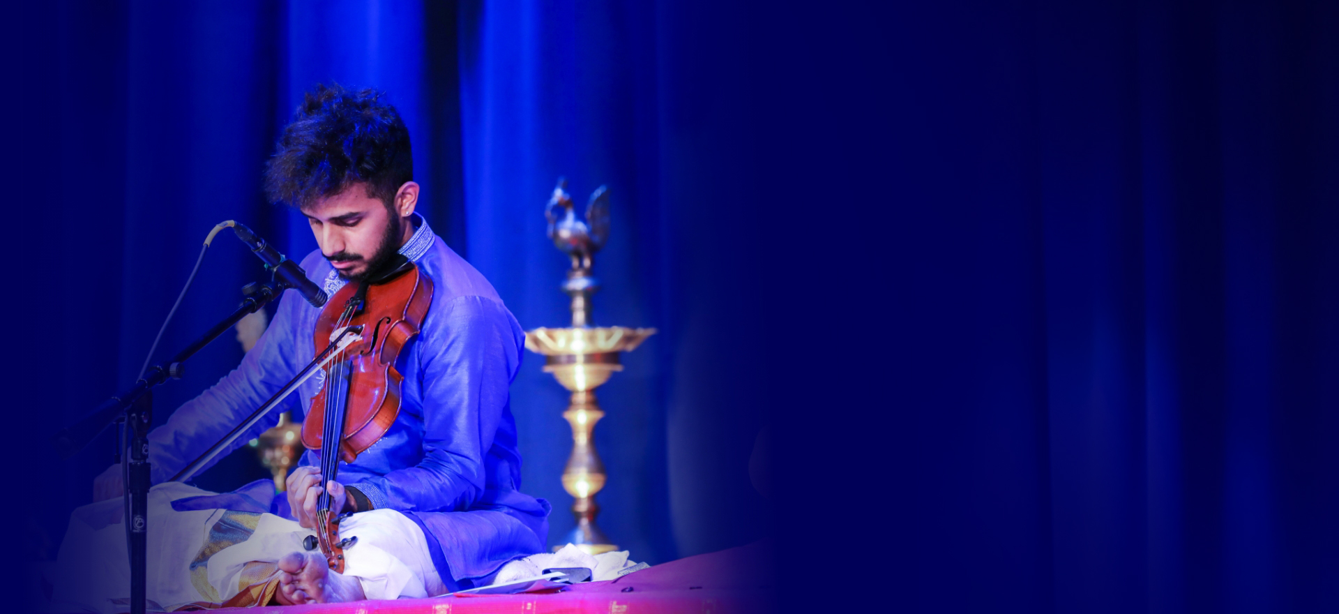 Achi Bala performing violin on a blue-lit concert stage